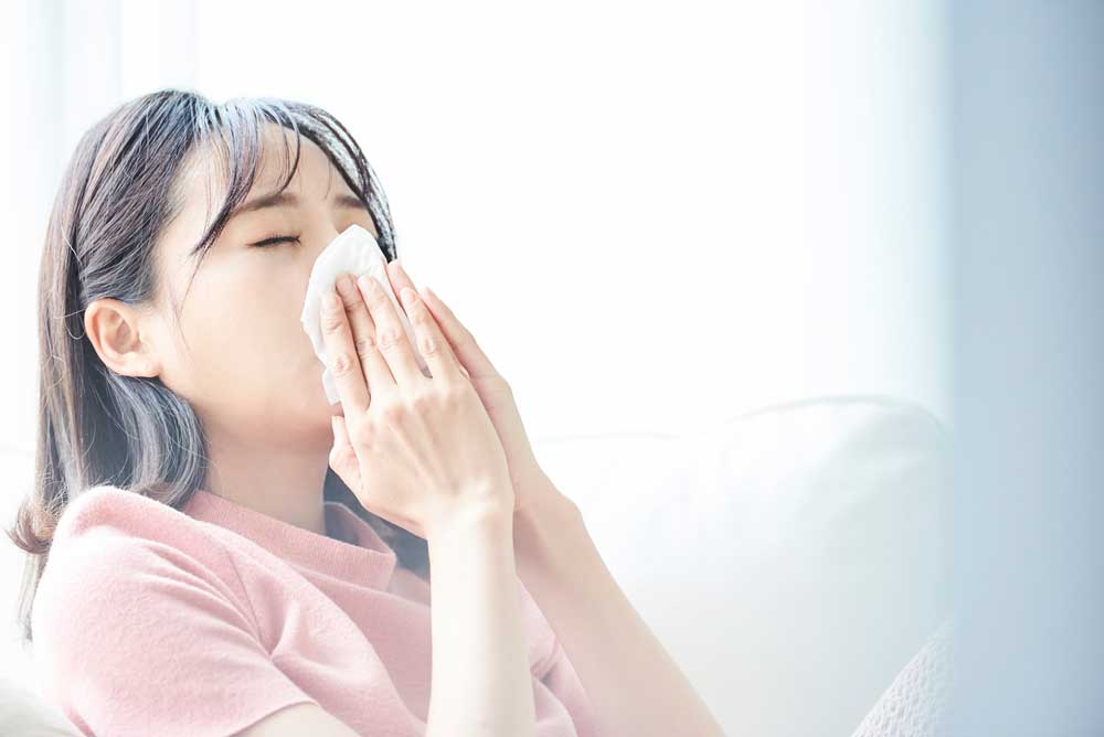 花粉症やアレルギー性鼻炎の症状がつらく、ティッシュで優しく鼻をかんでいる女性のイメージ。喉の乾燥や渇き対策の解説